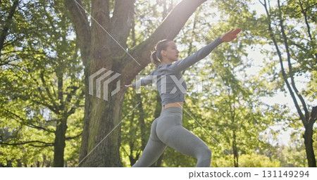 young beautiful white girl doing yoga in park among trees in clearing on summer day 131149294