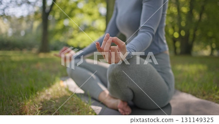 A young beautiful white girl practices yoga in the park and meditates in the lotus position among the trees in a clearing on a summer day A young beautiful white girl practices yoga in the park and meditates in the lotus position among the trees in a clearing on a summer day 131149325