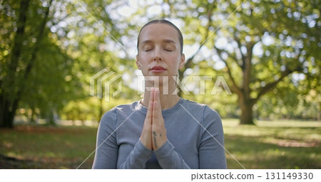 A young beautiful white girl practices yoga in the park and meditates in the lotus position among the trees in a clearing on a summer day A young beautiful white girl practices yoga in the park and meditates in the lotus position among the trees in a clearing on a summer day 131149330