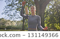 A young beautiful white girl practices yoga in the park and meditates in the lotus position among the trees in a clearing on a summer day and uses bamboo bells 131149366