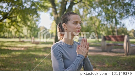 A young beautiful white girl practices yoga in the park and meditates in the lotus position among the trees in a clearing on a summer day 131149379