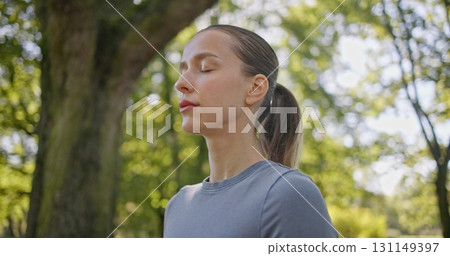 A young beautiful white girl practices yoga in the park and meditates in the lotus position among the trees in a clearing on a summer day 131149397