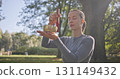 A young beautiful white girl doing yoga in the park and meditating in the lotus position among the trees in a clearing on a summer day and using a singing brass bowl 131149432