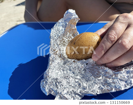 Woman wraps potatoes in foil for cooking over fire in barbecue grill. Outdoor camping, picnic preparation and rustic food Woman wraps potatoes in foil for cooking over fire in barbecue grill. Outdoor camping, picnic preparation and rustic food 131150669