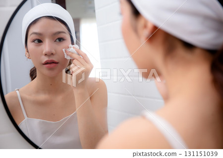 Beautiful young asian woman gently clean on face while looking mirror in bathroom. Beautiful young asian woman gently clean on face while looking mirror in bathroom. 131151039