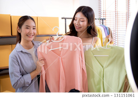 Two young asian woman live streaming online clothing store while showing clothing with smartphone. Two young asian woman live streaming online clothing store while showing clothing with smartphone. 131151061