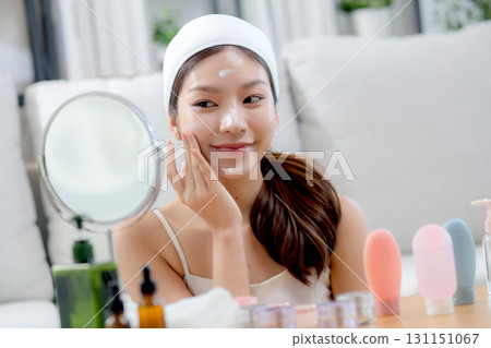 Beauty young asian woman applying cream on facial for wrinkles while looking mirror in living room. Beauty young asian woman applying cream on facial for wrinkles while looking mirror in living room. 131151067