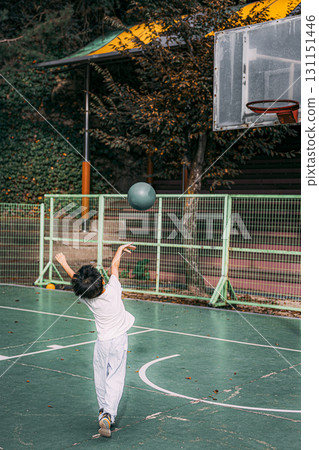 A young boy holding a green basketball and shooting at the goal. A moment. Back view. 131151446