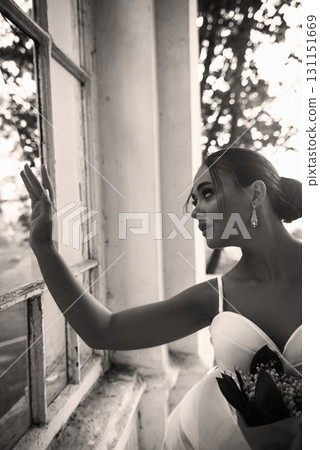 A beautiful girl in a white dress with a bouquet of lilies of the valley stands near the window A beautiful girl in a white dress with a bouquet of lilies of the valley stands near the window 131151669