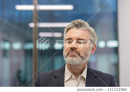 Businessman with closed eyes meditating, finding relaxation and balance, improving mental health and practicing mindfulness in a modern office environment 131152960