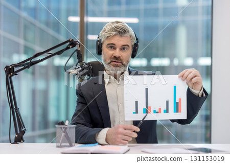 Businessman with headphones discussing financial report, pointing to a bar chart during an online webinar from a modern office, creating engaging digital content 131153019