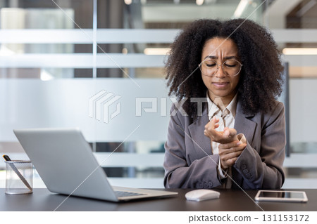 Young African American businesswoman working in the office at a notebook, holding her wrist and feeling severe pain. 131153172