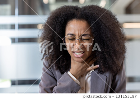 Close-up photo of an African American businesswoman sitting in an office and holding her hand to her throat, suffering from pain. Close-up photo of an African American businesswoman sitting in an office and holding her hand to her throat, suffering from pain. 131153187