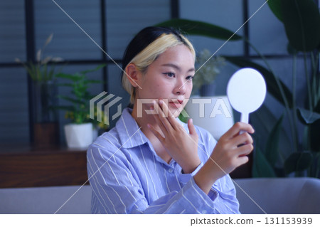 Young Asian women looking at mirror and concern about facial skin texture, dark spots and acne. Young Asian women looking at mirror and concern about facial skin texture, dark spots and acne. 131153939