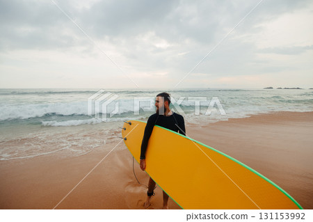 Young  bearded man with surfboard standing near a beach. Man with surfing board outdoors on a summer day. 131153992