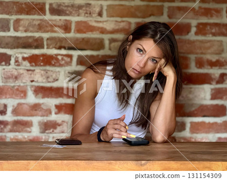 A thoughtful woman deeply pondering over important calculations in a rustic brickstyle environment A thoughtful woman deeply pondering over important calculations in a rustic brickstyle environment 131154309
