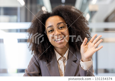 Close-up portrait of a young African American woman in a suit sitting in an office at a workplace, talking and waving her hand at the camera. Close-up portrait of a young African American woman in a suit sitting in an office at a workplace, talking and waving her hand at the camera. 131154374
