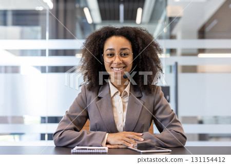 Portrait of a young smiling African American woman sitting behind a desk in a headset and looking confidently at the camera. 131154412