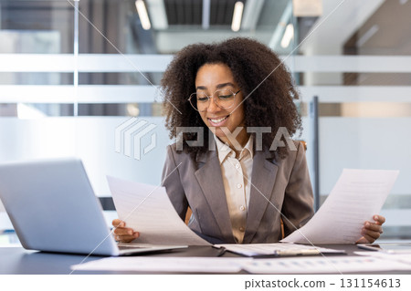 African-American young businesswoman lawyer working in office, sitting at table with laptop and studying documents. 131154613