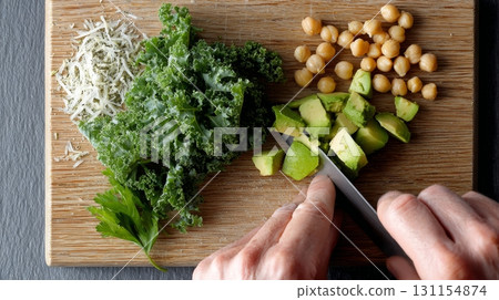 Hands chop avocado and kale on a wooden board for a nutritious, fiber-packed dish today Hands chop avocado and kale on a wooden board for a nutritious, fiber-packed dish today 131154874