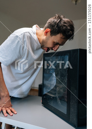 Vertical shot of computer technician male licking a dusty computer case with funny and frustrated expression, highlighting challenges of computer maintenance and repair. Concept of desktop PC service. 131155026