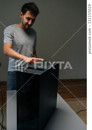 Vertical portrait of technician pointing at thick dust layer covering computer case, demonstrating potential hardware damage from neglecting regular maintenance. Concept of service, cleaning PC. 131155029