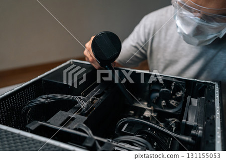 Computer technician wearing face mask and protective glasses using vacuum cleaner to remove dust and debris from inside computer case, ensuring optimal performance and preventing overheating. Computer technician wearing face mask and protective glasses using vacuum cleaner to remove dust and debris from inside computer case, ensuring optimal performance and preventing overheating. 131155053