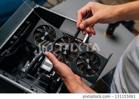 Technician cleaning graphics card with brush, performing essential maintenance on computer hardware to ensure optimal performance. Concept of computer hardware, repairing, upgrade and technology. 131155061