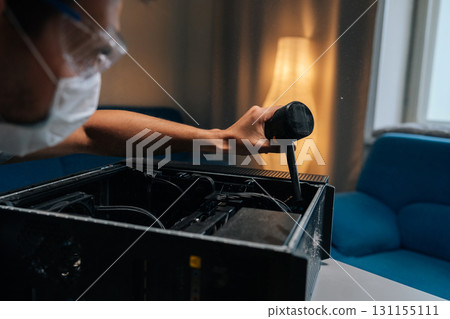 Close-up of technician in face mask and safety glasses cleaning computer case using small vacuum cleaner, demonstrating proper maintenance procedures. Concept of service, repair and cleaning computer Close-up of technician in face mask and safety glasses cleaning computer case using small vacuum cleaner, demonstrating proper maintenance procedures. Concept of service, repair and cleaning computer 131155111