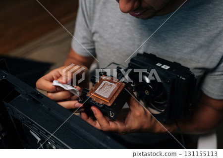 Precise computer maintenance involving cleaning processor cooling system, wiping delicate electronic components with white microfiber cloth for peak hardware performance at workshop. 131155113