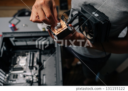 Unrecognizable computer technician wiping processor heatsink with microfiber cloth, removing dust and preparing hardware for precise system reassembly. Concept of computer hardware, repairing, upgrade 131155122