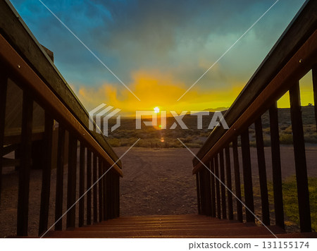 Golden sun setting over a serene valley, casting warm colors and shadows on wooden steps leading towards nature's beauty Golden sun setting over a serene valley, casting warm colors and shadows on wooden steps leading towards nature's beauty 131155174