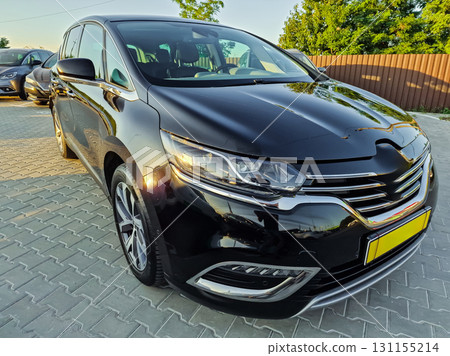 Sleek black car parked under the golden hour light in a serene outdoor setting with greenery and wooden fence in the background Sleek black car parked under the golden hour light in a serene outdoor setting with greenery and wooden fence in the background 131155214