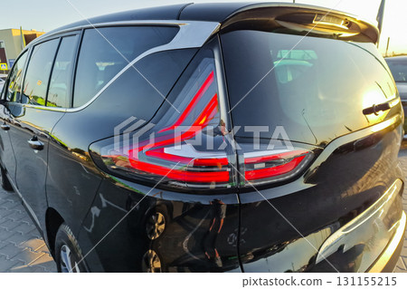 Sleek black minivan with eye-catching taillights parked at sunset, showcasing modern design details and reflecting warm golden hues Sleek black minivan with eye-catching taillights parked at sunset, showcasing modern design details and reflecting warm golden hues 131155215