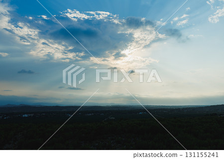 Bright rays of sunlight pierce through the clouds over a serene landscape at dusk 131155241