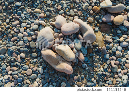 Brightly colored pebbles scattered on a sandy beach in the warm sunlight during a serene summer afternoon with gentle waves nearby creating a peaceful atmosphere 131155246