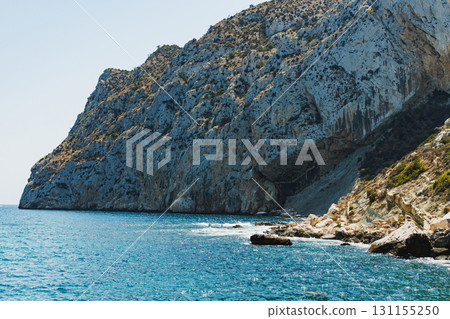 Sunlight dances on the waves as cliffs rise majestically above the turquoise sea in a serene coastal landscape near a hidden beach 131155250