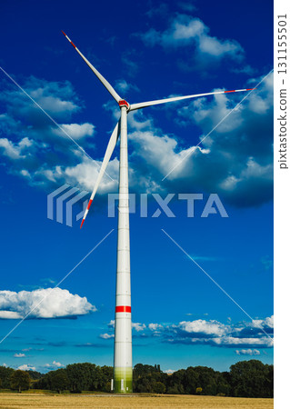 Majestic wind turbine stands tall against a vibrant blue sky, embodying renewable energy amidst a serene landscape 131155501