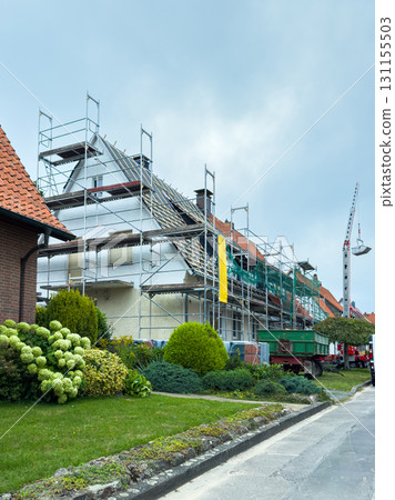 Construction work in progress on a residential building under overcast skies, showcasing scaffolding and landscaping efforts in a quiet neighborhood Construction work in progress on a residential building under overcast skies, showcasing scaffolding and landscaping efforts in a quiet neighborhood 131155503