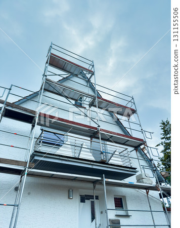 Renovation of a charming white house under cloudy skies with scaffolding in place 131155506