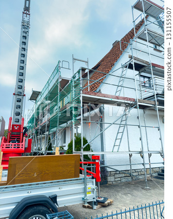 Construction workers enhance a charming home with scaffolding and advanced equipment on a cloudy day 131155507