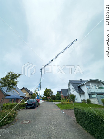 Construction crane towers over residential area during cloudy day with nearby homes and parked vehicle in view 131155521
