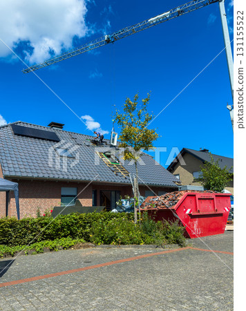 Roof renovation in a suburban neighborhood under clear blue skies with a crane and dumpster present 131155522