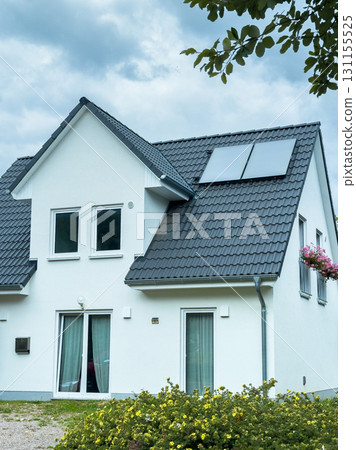 Modern white house with solar panels surrounded by greenery on a partly cloudy day near a community Modern white house with solar panels surrounded by greenery on a partly cloudy day near a community 131155525