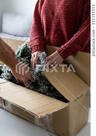 Young couple unpacking Artificial Christmas Tree from Storage Box at home 131155553