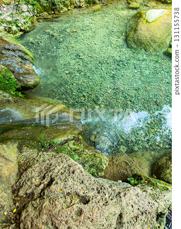 Crystal clear water flows over rocks in a serene natural setting surrounded by lush greenery in a tranquil forest Crystal clear water flows over rocks in a serene natural setting surrounded by lush greenery in a tranquil forest 131155738