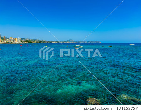 Vibrant blue waters and boats dotting the coastline of a sunny beach in a scenic location during a clear summer day Vibrant blue waters and boats dotting the coastline of a sunny beach in a scenic location during a clear summer day 131155757