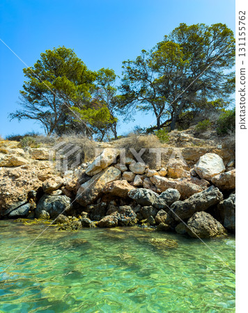Serene coastal scene with clear turquoise water and rocky shore under bright blue sky in summer Serene coastal scene with clear turquoise water and rocky shore under bright blue sky in summer 131155762