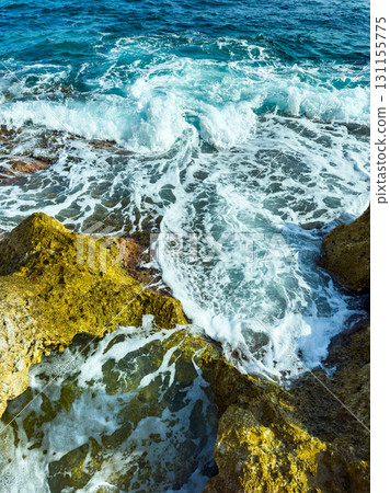 Waves dance over rocky shore under bright blue sky during midday sun, showcasing nature's beauty and energy in a coastal paradise Waves dance over rocky shore under bright blue sky during midday sun, showcasing nature's beauty and energy in a coastal paradise 131155775