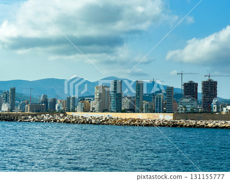Construction and development along the shoreline of a coastal city under a blue sky with mountains in the distance Construction and development along the shoreline of a coastal city under a blue sky with mountains in the distance 131155777